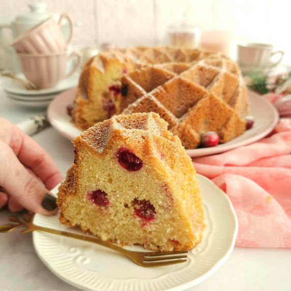 Shot of table with a slice of cranberry Madeira bundt cake & larger cake to background
