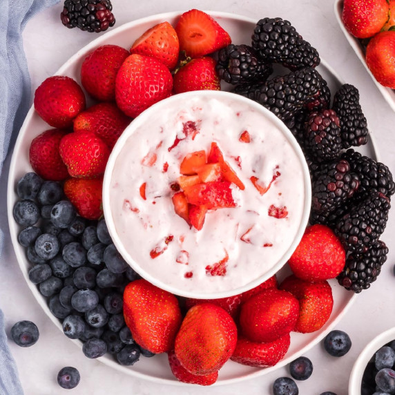 Cream cheese fruit dip topped with strawberry bits and surrounded by a platter of berries to dip.