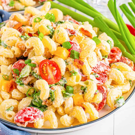 Zoomed in on creamy bacon ranch pasta salad on a plate with green onions near the plate.