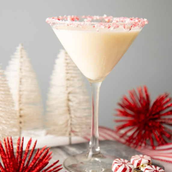 A creamy peppermint martini in a martini glass with a crushed candy cane rim by red and white decor.