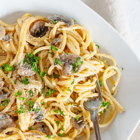 creamy mushroom pasta on a white plate with fork on a white kitchen towel 