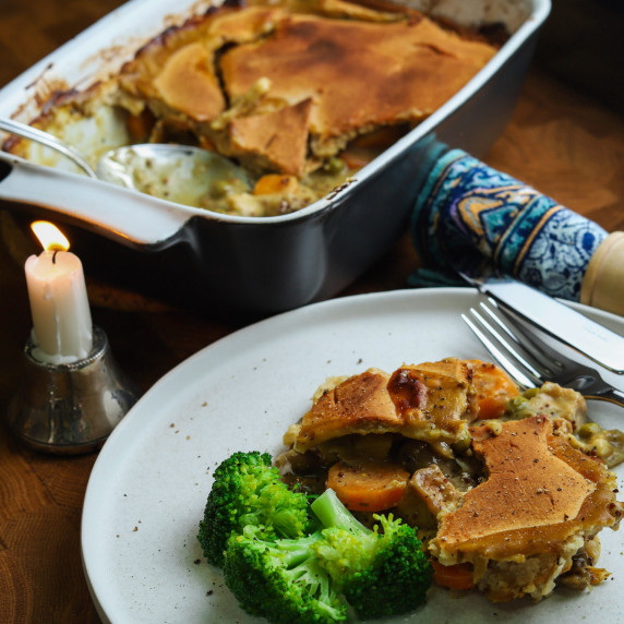 Photo of a plate of pie with the main pie dish in the background and a candle burning.