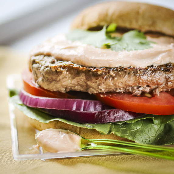 Side close up shot of a burger assembled with sriracha sauce on top without the top bun.