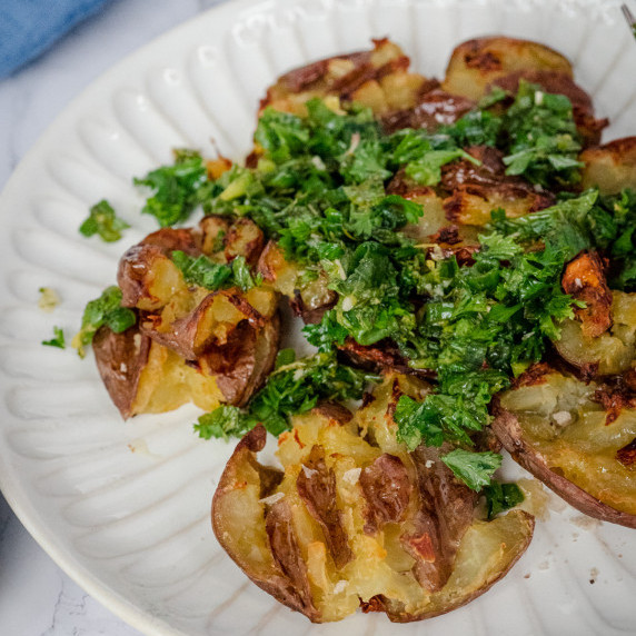 crispy smashed potatoes topped with garlic herbs chimichurri on a white plate.