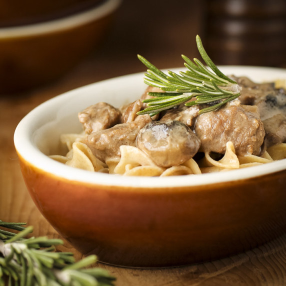 Side shot of crockpot beef stroganoff garnished with rosemary in an orange oval bowl.