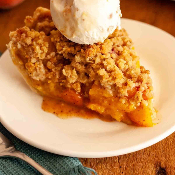 A close up of a slice of crumble top peach pie topped with ice cream.