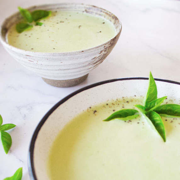 two bowls of cucumber soup sit on a white counter. 
