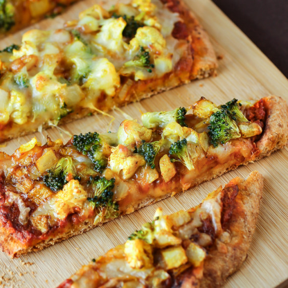 Side view of multiple slices of curry pizza on a wooden cutting board