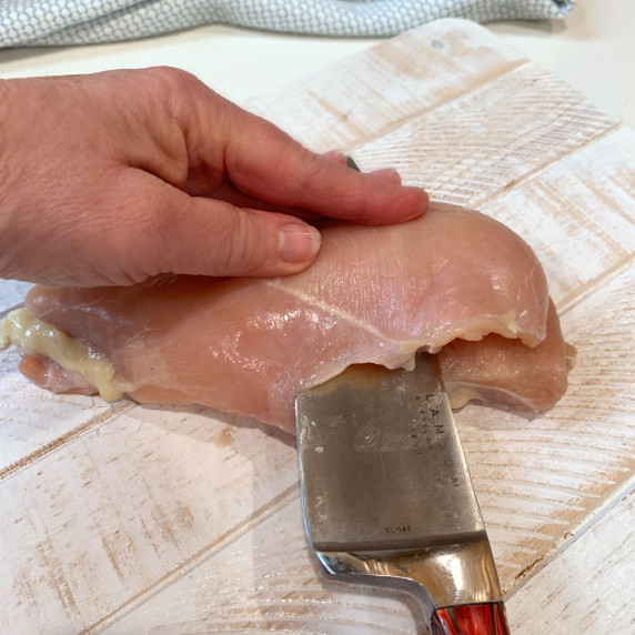 Cutting a chicken breast in half with a chefs knife.