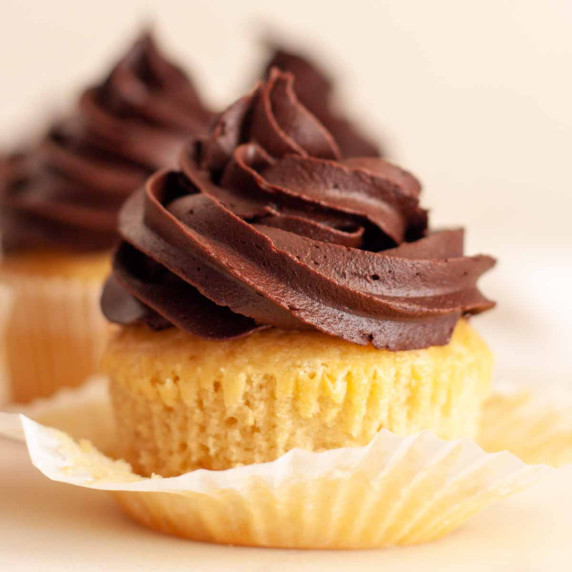 A closeup of a vanilla cupcake topped with dairy free chocolate frosting.