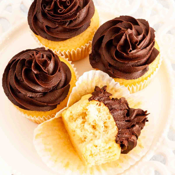 Four dairy free vanilla cupcakes with chocolate frosting on a white plate.