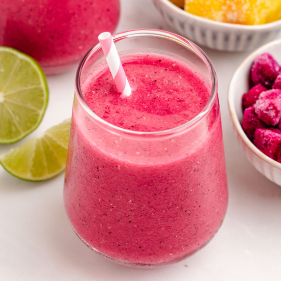 A dragon fruit mango smoothie in a glass with a straw with a lime in the background.