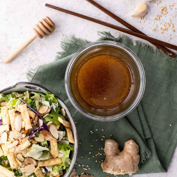 Overhead of a glass jar with homemade sesame ginger dressing alongside an asian-inspired salad.