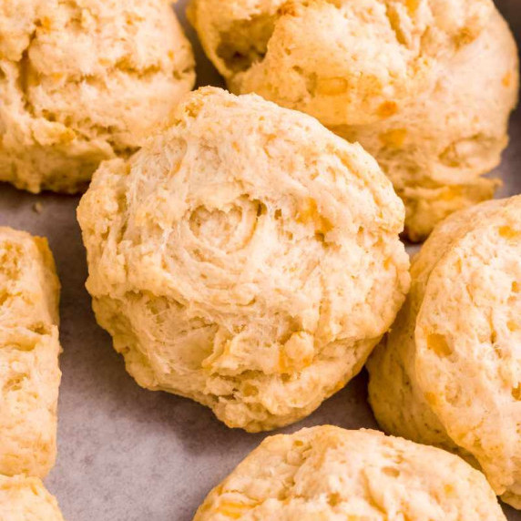 Close view of fluffy, cheesy drop biscuits nestled together on a parchment paper lines serving tray.