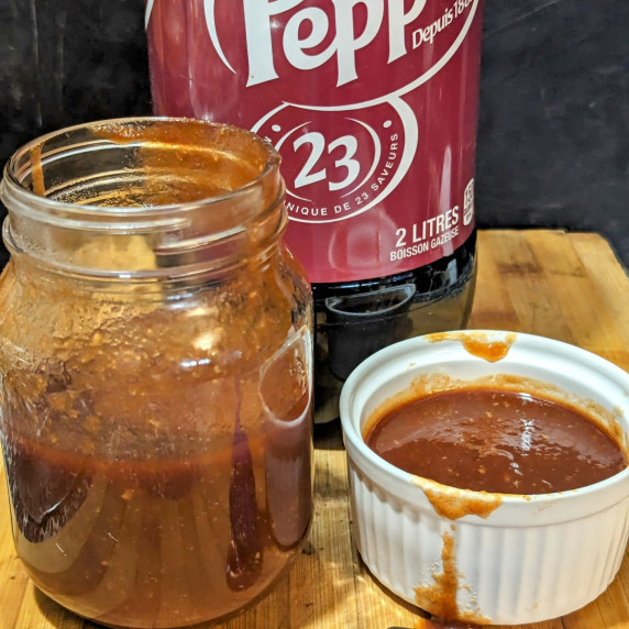 A bowl of Dr Pepper Rib Sauce with a mason jar of sauce and a bottle of Dr Pepper