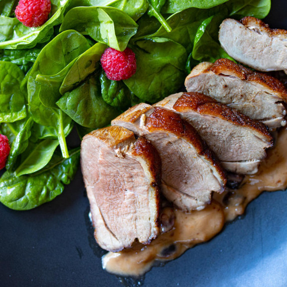 sliced duck breast with spinach salad and raspberries on a black palte