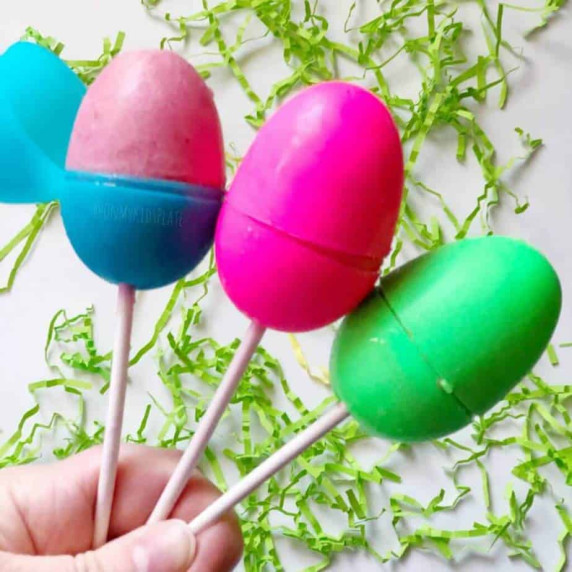 Three Easter eggs on top of sticks filled with frozen popsicle filling are held by a hand