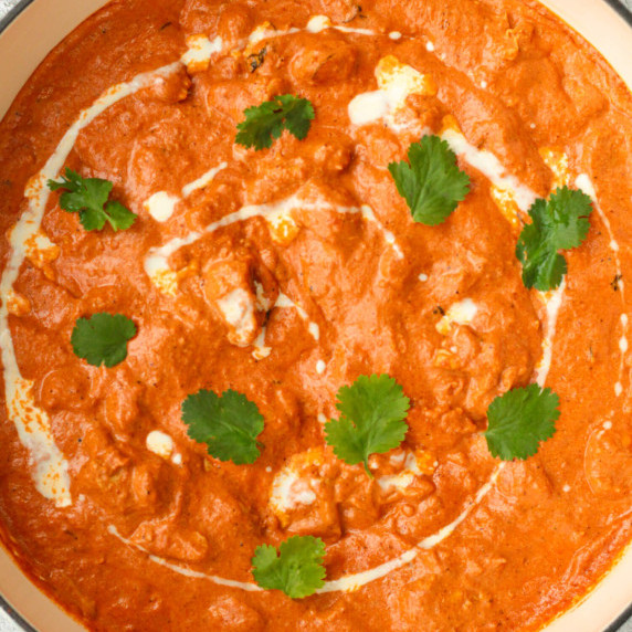 Butter chicken dish in a large pan with drizzle of double cream and coriander