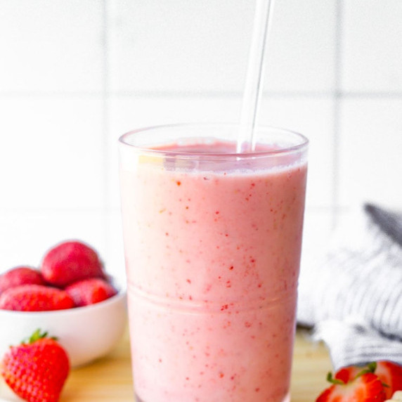 A strawberry banana smoothie sits on a counter with fresh strawberries.