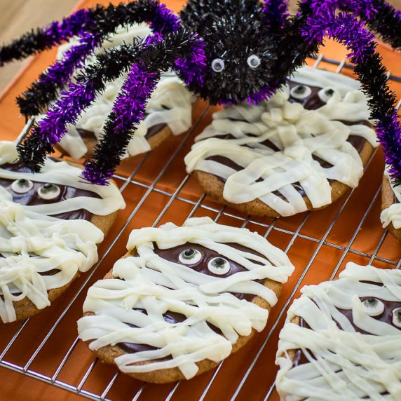 Side angled view of multiple mummy cookies on a cooling rack with a purple and black decorative spid
