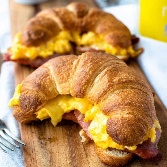 Two croissants filled with egg, bacon and cheese on a wooden board.