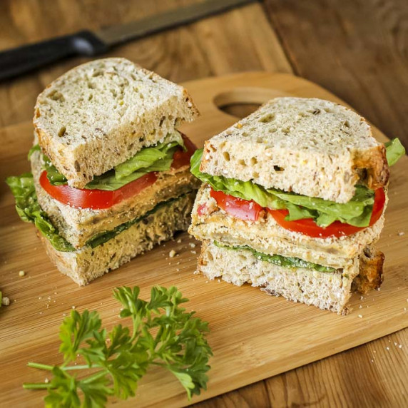 Side shot of a milanese sandwich cut in half on a wooden cutting board with herbs on the side.