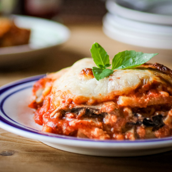 Side shot of eggplant polenta lasagna garnished with basil on a white and blue plate.