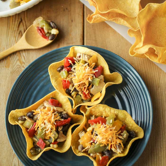 Overhead shot of three tortilla bowls on a blue plate with more empty tortilla bowls in the back.