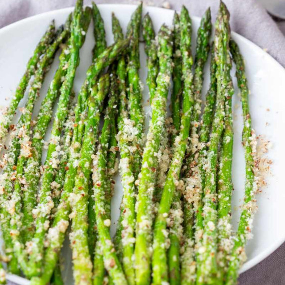 Tender oven roasted asparagus topped with nutty parmesan cheese arranged on a white serving platter.