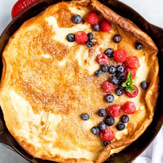 A finnish oven pancake in an enameled cast iron skillet topped with fresh berries and powdered sugar