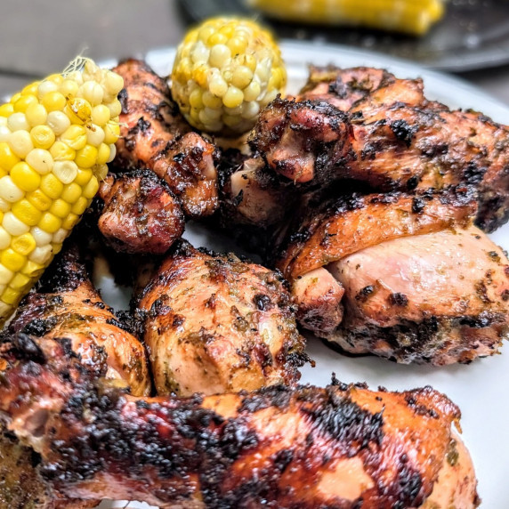 Fire-grilled jerk marinated chicken on a plate with corn on the cob