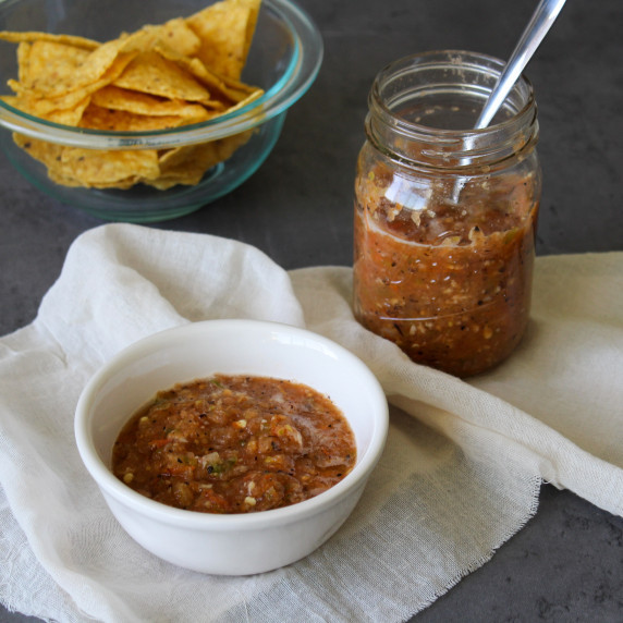 A jar and bowl of homemade fire roasted salsa plus tortilla chips for serving
