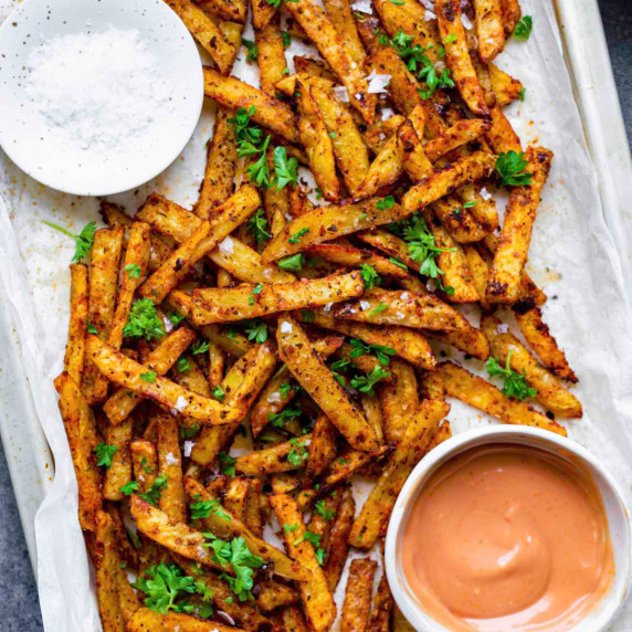 Cajun fries served on a baking sheet layered with parchment paper, and topped with chopped parsley.