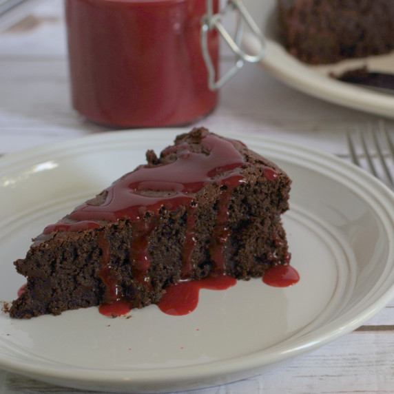 Flourless chocolate cake slice on a plate and topped with raspberry sauce