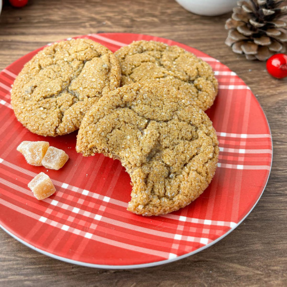 Fresh ginger cookies on a red and white plaid plate, one with a bite missing.