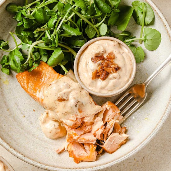 Air fried salmon, bacon aioli and greens in ramekin on white plate with fork