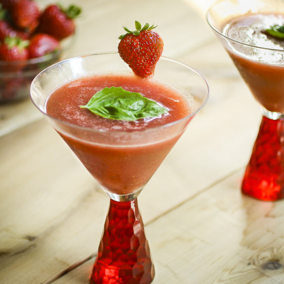 Side view of frozen strawberry basil margaritas garnished with basil and strawberries in a red glass
