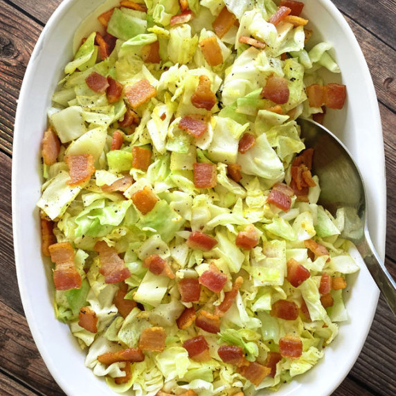 Bacon Fried Cabbage in a white serving dish with a silver serving spoon.