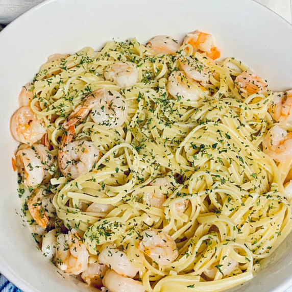 Shrimp scampi in a white bowl on a blue and white dish towel on kitchen table.  