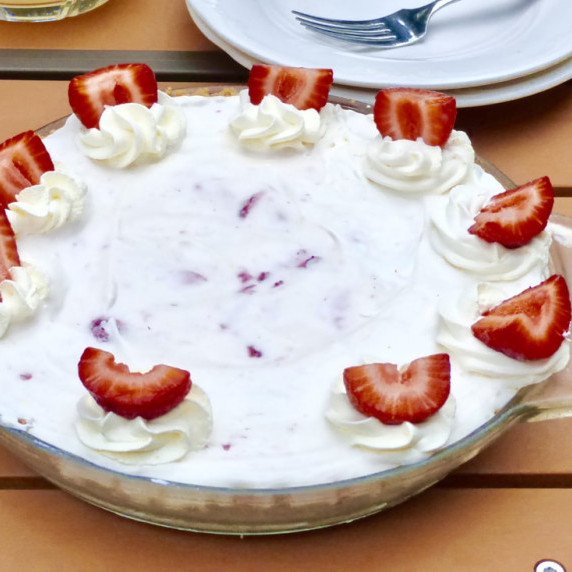 Strawberry ice cream pie with a pie server on a picnic table.  