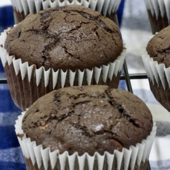 chocolate muffins on a baking rack with a blue and white tablecloth underneath.