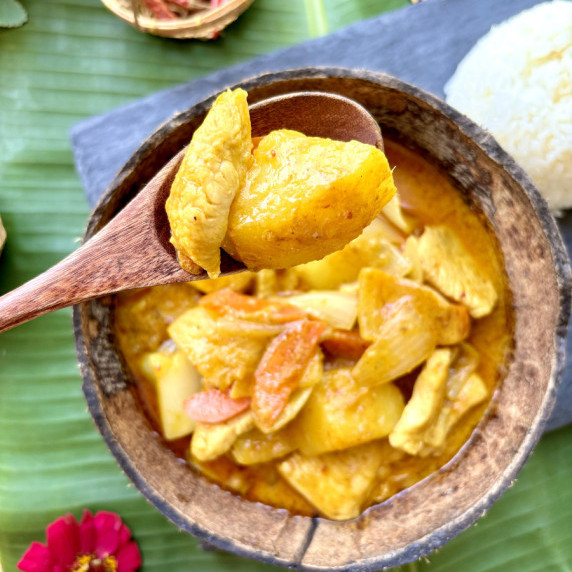 Top-view of Thai yellow chicken curry with a wooden spoon lifting a potato and chicken.