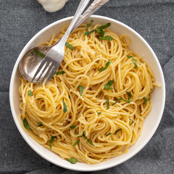 garlic butter pasta in a white bowl with a spoon and fork