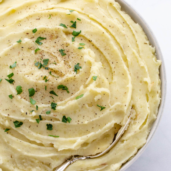 Mashed potatoes with coconut milk and rosemary roasted garlic in a bowl with a chopped parsley.