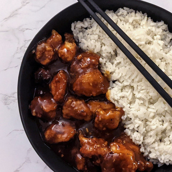 A bowl of crispy general Tso's chicken and rice with chopsticks