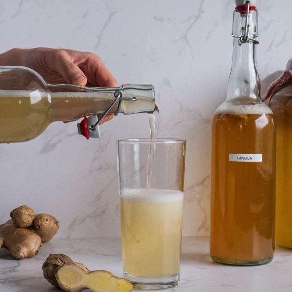 Someone pouring ginger kombucha in a glass