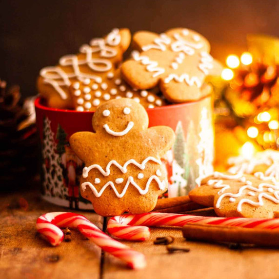 A closeup of gingerbread cookies on two candy canes next to a cookie box and christmas lights.