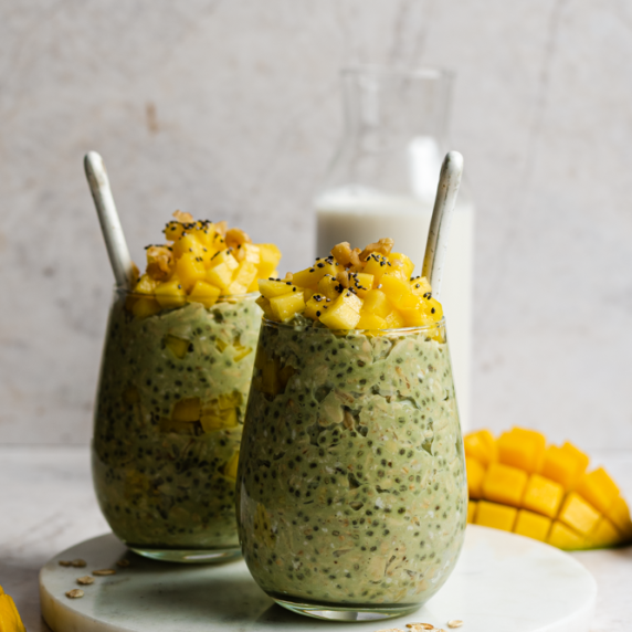 Mango matcha overnight oats arranged in a two aesthetic cups with straw and milk and mango