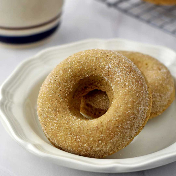 Two gluten free cinnamon sugar donuts on a round white dessert plate.