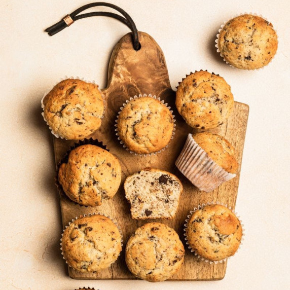 Top view of wooden cutting board with twelve almond flour banana muffins on a light background.